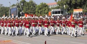 Members of the U.S. Navy, dressed in ceremonial uniforms, march in formation during a national parade in Washington, D.C., with crowds of spectators watching from the grandstands and a control center visible in the background.